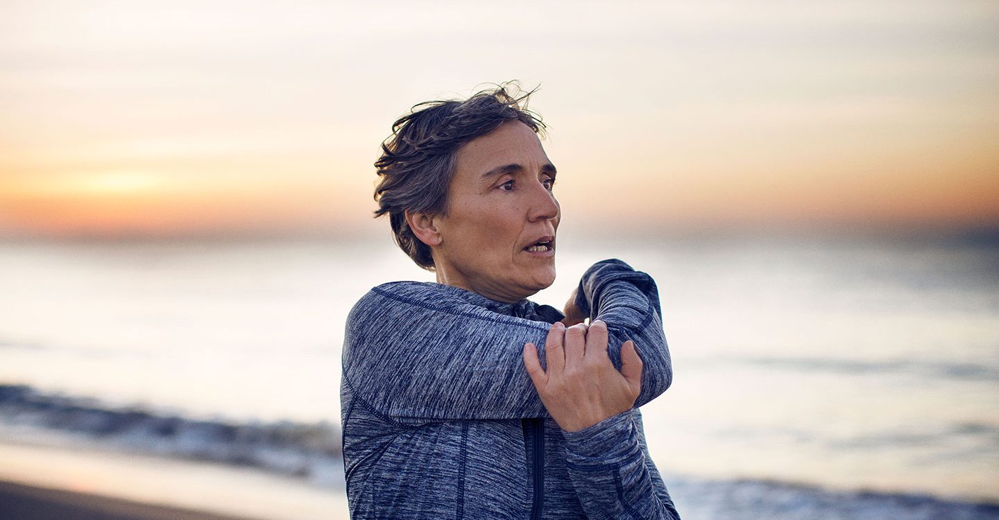 Mujer estirandose en la playa antes de hacer ejercicio y conocer el rol del colágeno en la salud