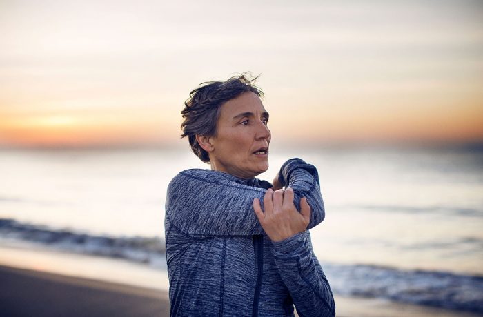 Mujer estirandose en la playa antes de hacer ejercicio y conocer el rol del colágeno en la salud